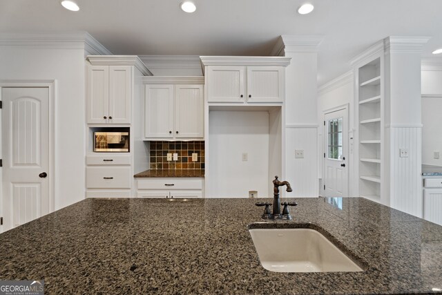 kitchen featuring white cabinetry, dark stone countertops, crown molding, and sink