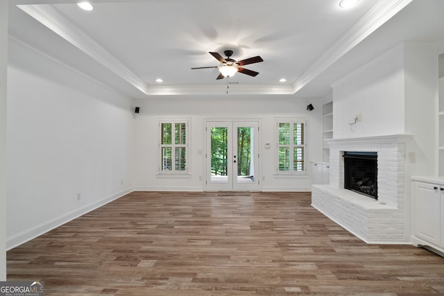 unfurnished living room featuring crown molding, ceiling fan, a brick fireplace, hardwood / wood-style floors, and a raised ceiling