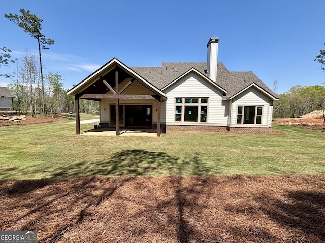 back of property with a patio, a shingled roof, a lawn, and a chimney