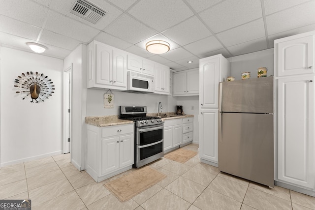 kitchen featuring white cabinetry, stainless steel appliances, a drop ceiling, and light tile patterned flooring