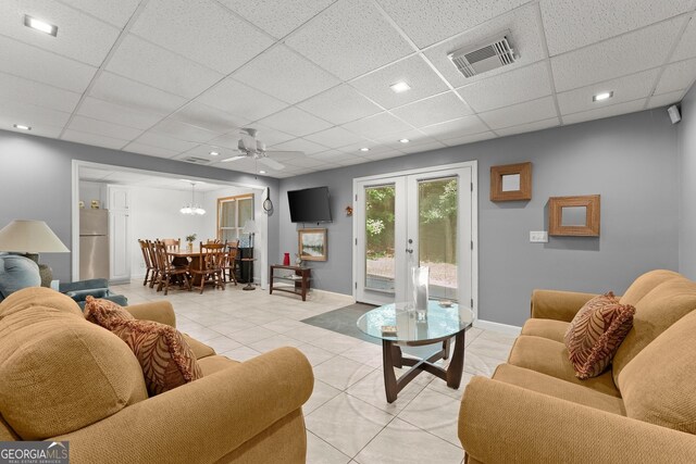 living room featuring a drop ceiling, light tile patterned floors, ceiling fan, and french doors