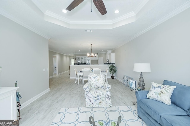 living room featuring ceiling fan with notable chandelier, light hardwood / wood-style flooring, crown molding, and a tray ceiling