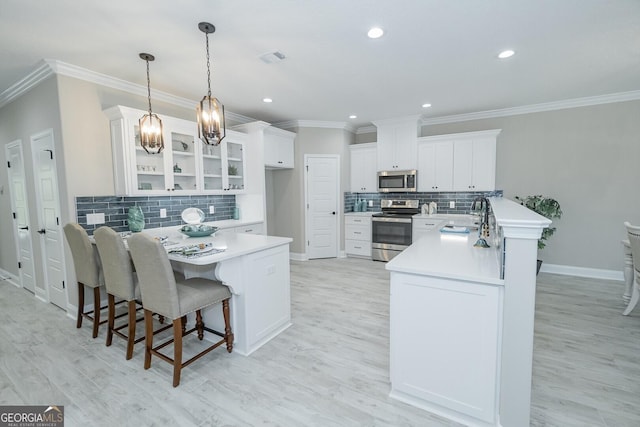 kitchen with white cabinetry, sink, hanging light fixtures, stainless steel appliances, and a kitchen bar