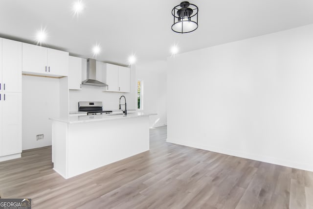 kitchen featuring a kitchen island with sink, light hardwood / wood-style flooring, wall chimney exhaust hood, stainless steel range oven, and white cabinetry