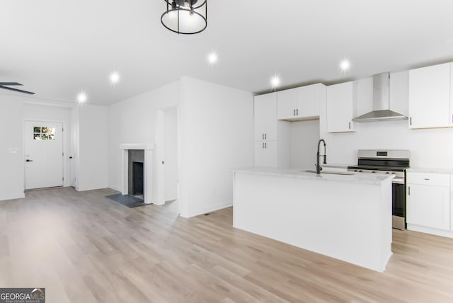 kitchen featuring white cabinetry, sink, wall chimney range hood, a kitchen island with sink, and stainless steel stove