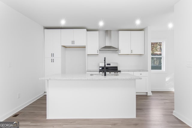 kitchen with white cabinets, a kitchen island with sink, and wall chimney range hood