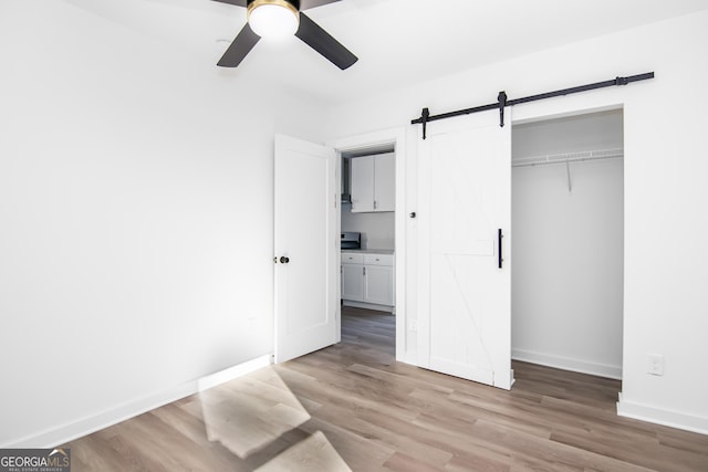 unfurnished bedroom with light wood-type flooring, a barn door, a closet, and ceiling fan