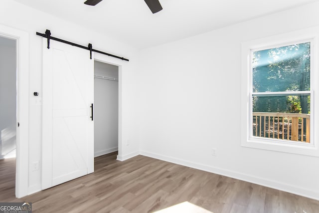 unfurnished bedroom featuring light wood-type flooring, a barn door, a closet, and ceiling fan