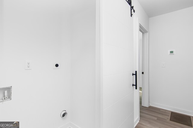 laundry room with hookup for a washing machine, a barn door, light hardwood / wood-style flooring, and electric dryer hookup