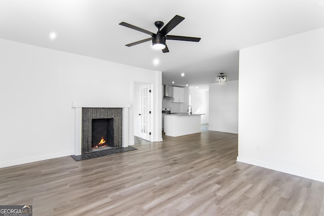 unfurnished living room featuring a fireplace, light hardwood / wood-style floors, ceiling fan, and sink