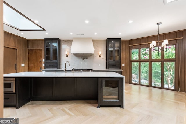 kitchen with light parquet floors, a kitchen island with sink, and premium range hood