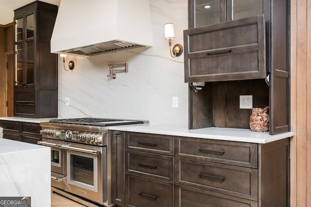 kitchen with dark brown cabinets, premium range hood, light stone counters, and range with two ovens