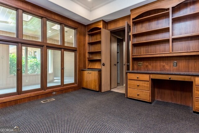 unfurnished office with dark colored carpet, built in shelves, built in desk, and ornamental molding