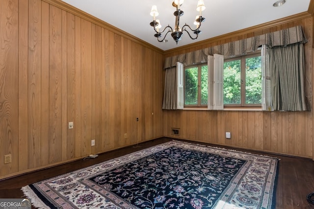 spare room featuring an inviting chandelier, crown molding, dark hardwood / wood-style floors, and wooden walls