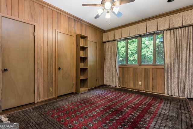 unfurnished bedroom featuring wooden walls, crown molding, and ceiling fan