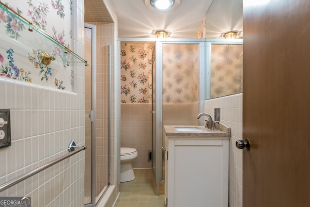 bathroom featuring a shower with door, toilet, vanity, tile walls, and tile patterned floors