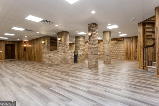 basement with brick wall, wooden walls, hardwood / wood-style flooring, and a drop ceiling