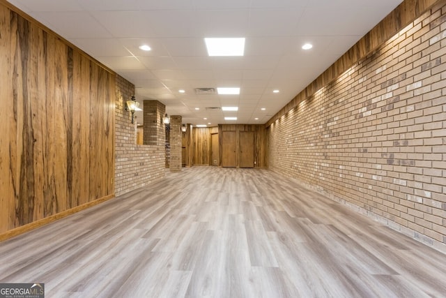 interior space with brick wall, wood walls, light wood-type flooring, and a paneled ceiling