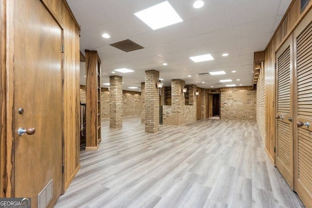 interior space with brick wall, light wood-type flooring, and a drop ceiling