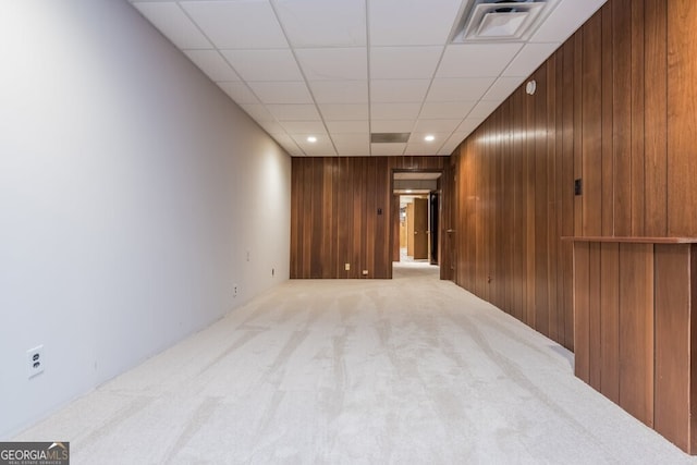 carpeted empty room featuring wooden walls and a paneled ceiling