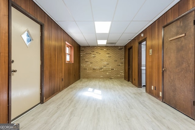 interior space with brick wall, light hardwood / wood-style floors, a drop ceiling, and wooden walls