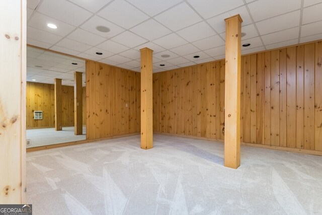 basement featuring wood walls, light carpet, and a drop ceiling