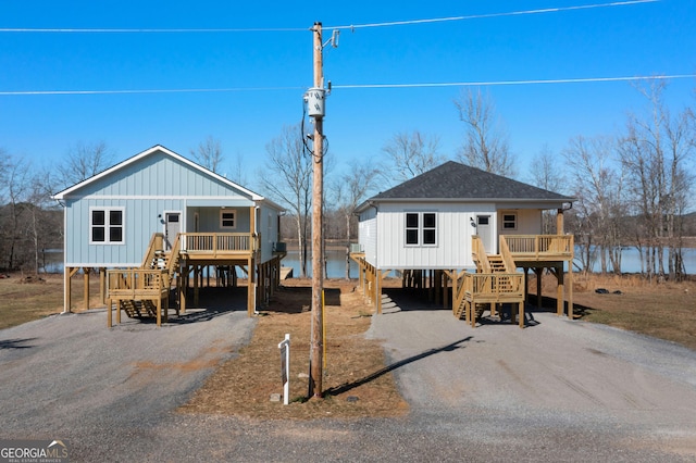 view of front of home with gravel driveway, roof with shingles, a porch, a carport, and stairs