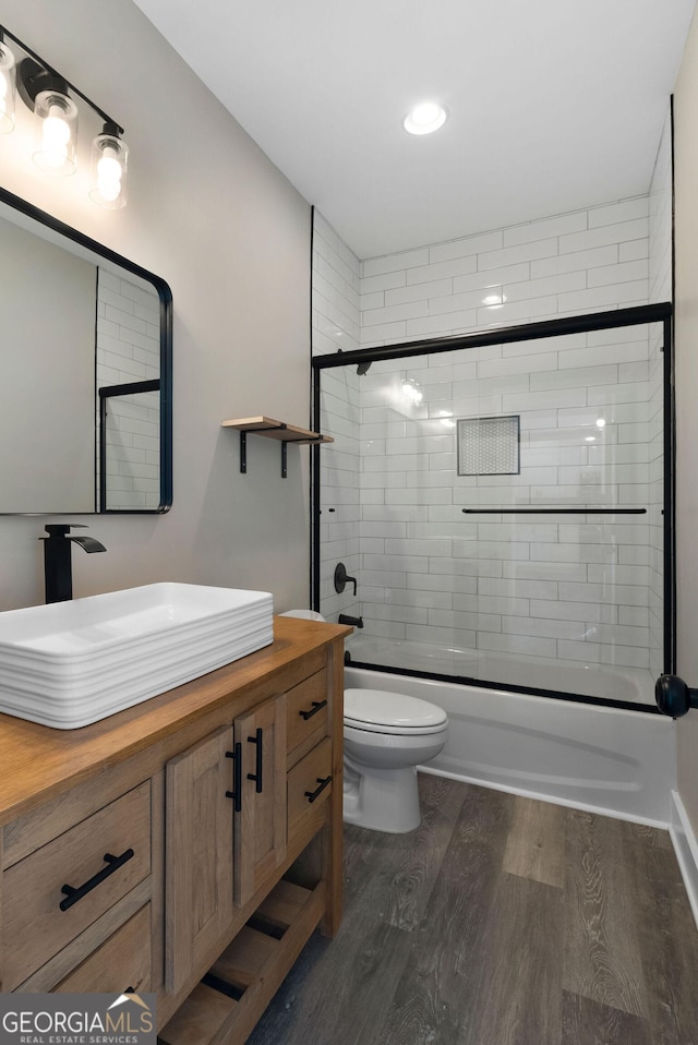 bathroom featuring vanity, combined bath / shower with glass door, wood finished floors, and toilet