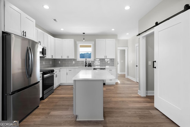 kitchen featuring appliances with stainless steel finishes, light countertops, white cabinetry, and a barn door