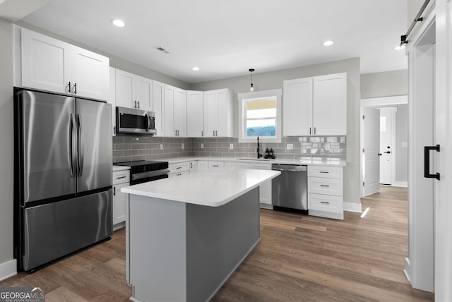 kitchen featuring a barn door, stainless steel appliances, dark wood-style flooring, a sink, and visible vents