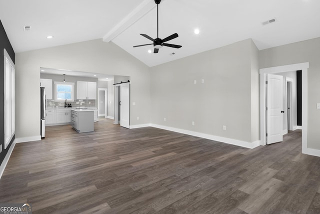 unfurnished living room featuring a barn door, dark wood-style flooring, visible vents, baseboards, and beam ceiling