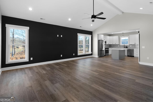 unfurnished living room with baseboards, dark wood finished floors, a ceiling fan, high vaulted ceiling, and beam ceiling