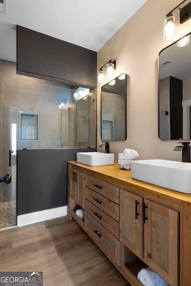 full bathroom featuring double vanity, a shower stall, a sink, and wood finished floors