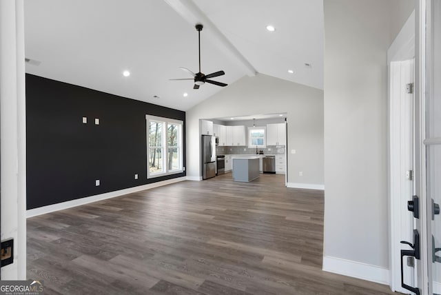 unfurnished living room featuring a ceiling fan, baseboards, dark wood-type flooring, and beam ceiling