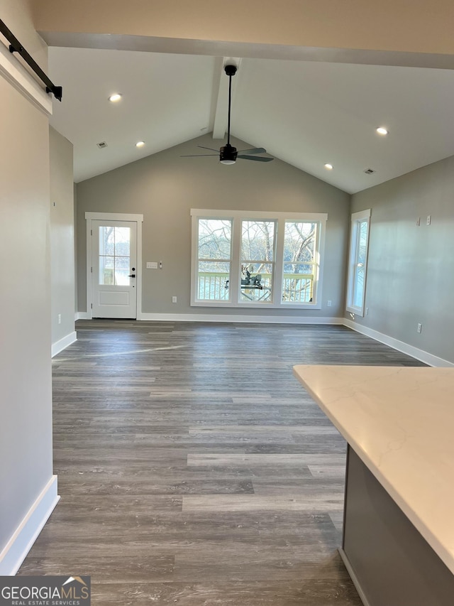 unfurnished living room featuring dark hardwood / wood-style flooring, a barn door, ceiling fan, and vaulted ceiling with beams