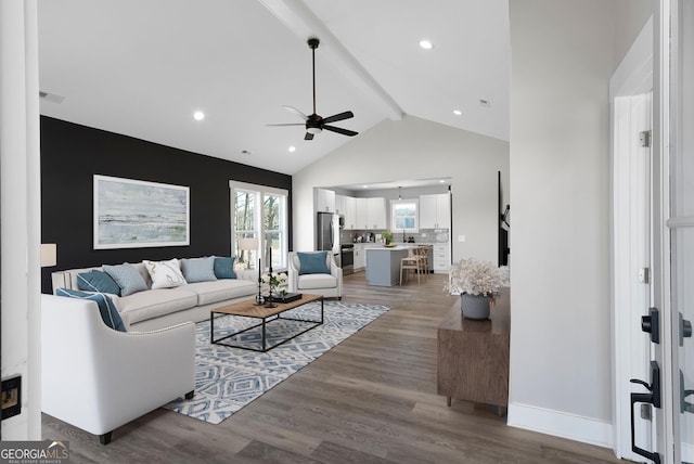 living room with ceiling fan, high vaulted ceiling, wood finished floors, baseboards, and beamed ceiling