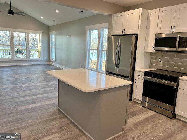 kitchen with decorative backsplash, appliances with stainless steel finishes, a kitchen island, ceiling fan, and white cabinetry