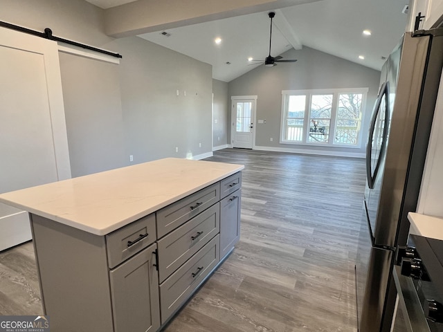 kitchen with stainless steel fridge, gray cabinetry, a barn door, beamed ceiling, and a center island