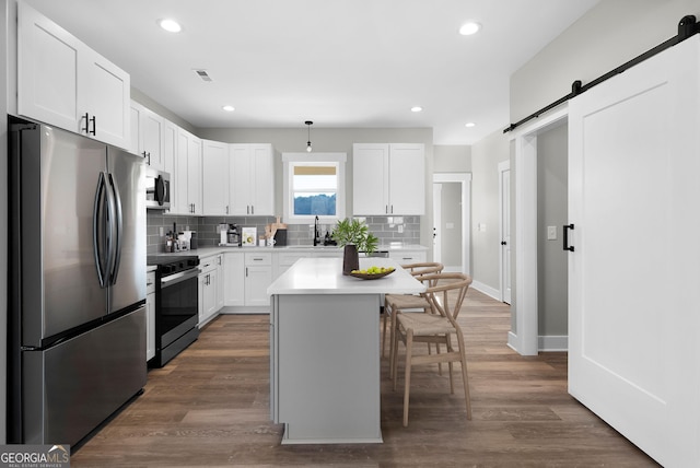 kitchen featuring stainless steel appliances, a barn door, a kitchen bar, and white cabinetry