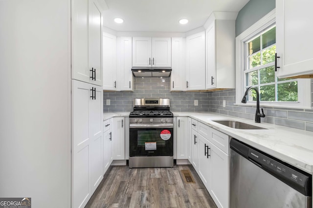 kitchen with stainless steel appliances, white cabinets, sink, light stone counters, and hardwood / wood-style flooring