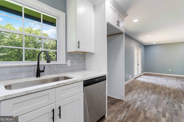 kitchen featuring stainless steel dishwasher, white cabinetry, decorative backsplash, light wood-type flooring, and light stone countertops