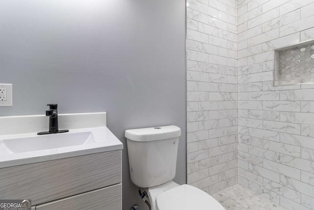 bathroom with tiled shower, toilet, and vanity