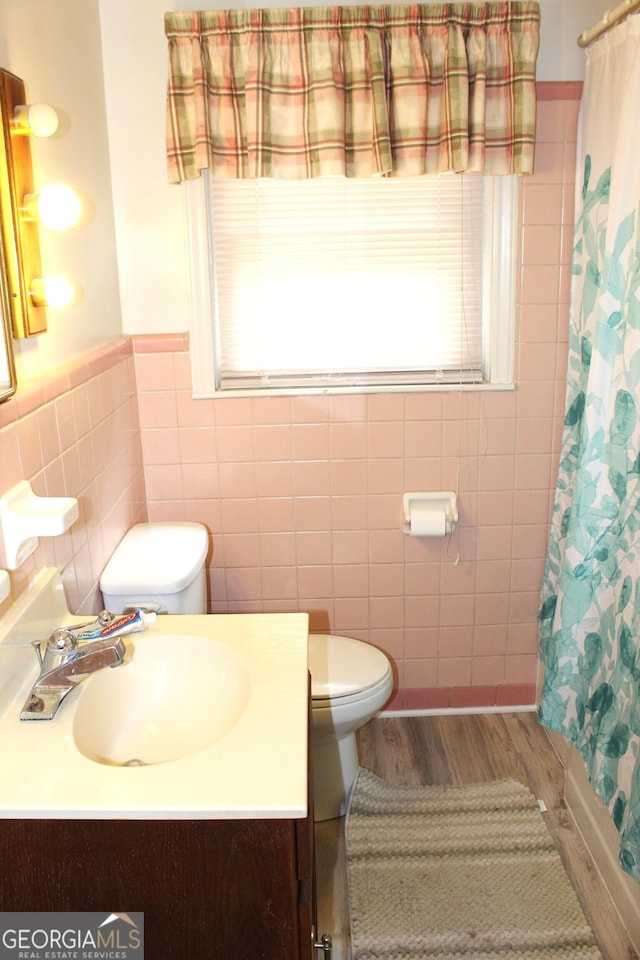 bathroom featuring wood-type flooring, tile walls, vanity, walk in shower, and toilet