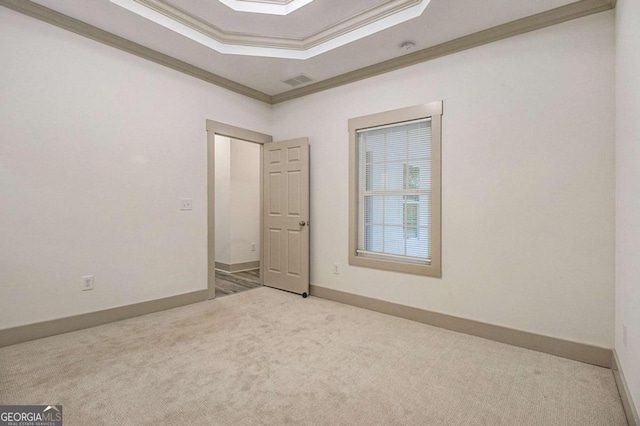 empty room featuring a raised ceiling, light carpet, and crown molding