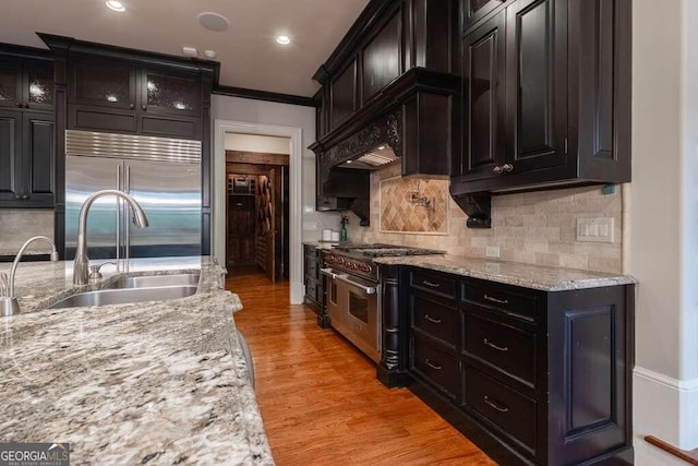 kitchen featuring sink, light stone counters, light wood-type flooring, premium appliances, and crown molding