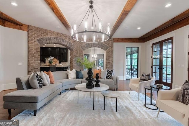 living room featuring a chandelier, brick wall, french doors, light wood-type flooring, and beamed ceiling