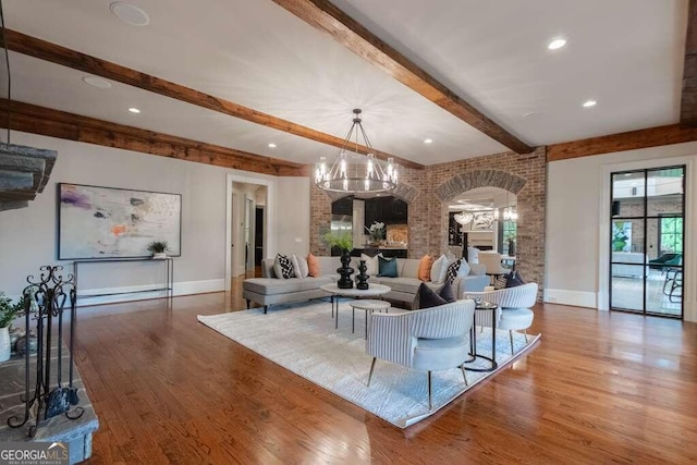 living room featuring a notable chandelier, beamed ceiling, brick wall, and wood-type flooring