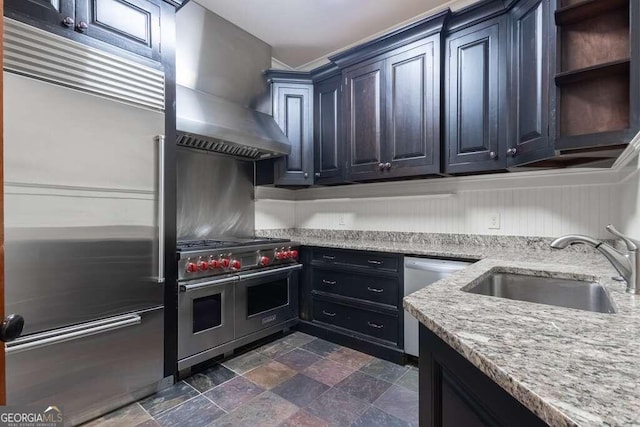 kitchen featuring sink, wall chimney range hood, light stone countertops, and premium appliances