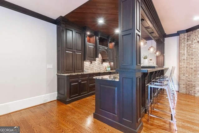 bar featuring light hardwood / wood-style floors, dark brown cabinets, ornamental molding, and decorative light fixtures