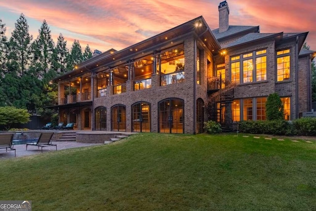 back house at dusk featuring a lawn, a patio area, and a balcony